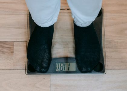 From above of crop unrecognizable plus size person in casual clothes standing on weighing scale on wooden floor