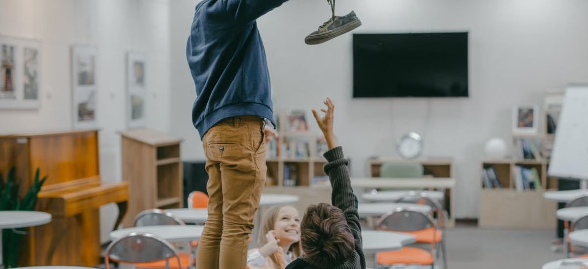Children interacting in a classroom setting, playfully reaching for an object.