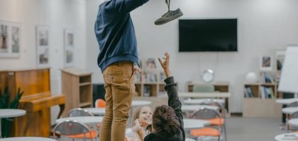 Children interacting in a classroom setting, playfully reaching for an object.