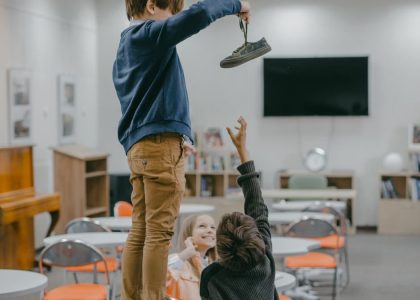 Children interacting in a classroom setting, playfully reaching for an object.