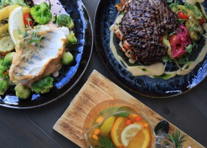 Top view of gourmet fish and steak dishes with fresh citrus and herbs on a stylish table setting.