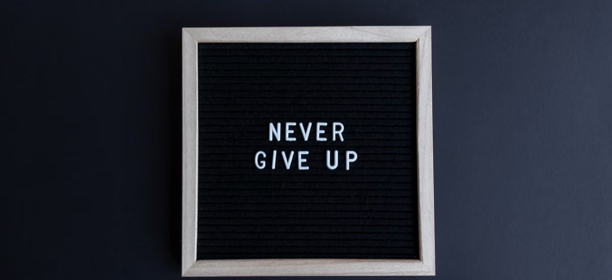 Inspirational letter board with 'Never Give Up' phrase on gray background.