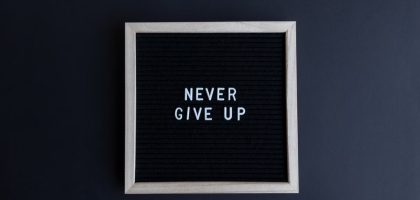 Inspirational letter board with 'Never Give Up' phrase on gray background.
