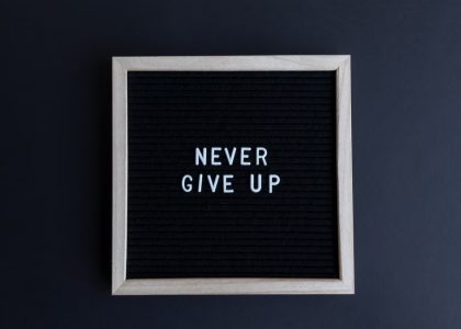 Inspirational letter board with 'Never Give Up' phrase on gray background.